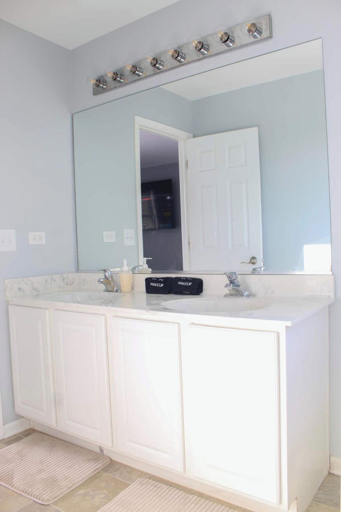 Une salle de bain avec un grand miroir, un meuble-lavabo blanc et un luminaire placé au-dessus du miroir.
