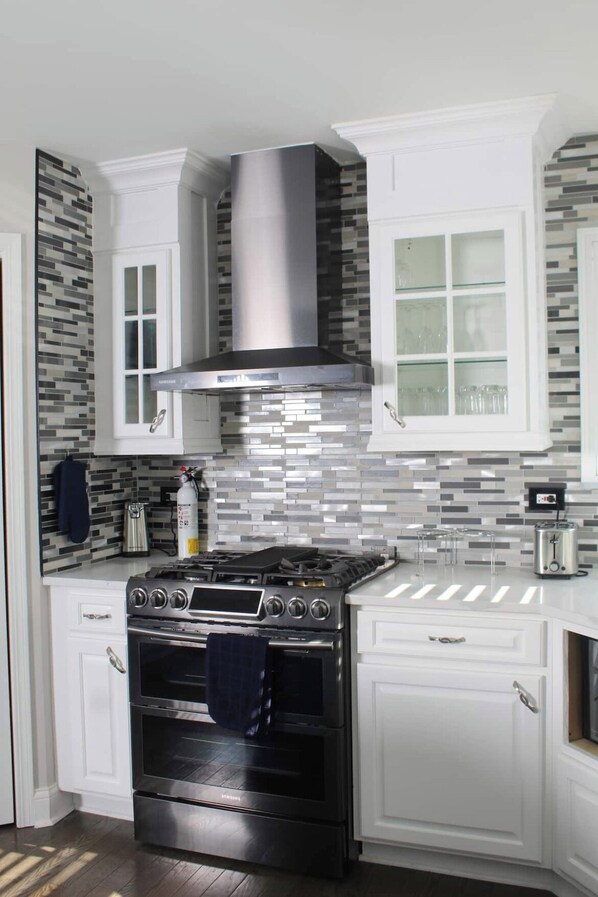 Kitchen features a stainless steel range hood, double oven, and tiled backsplash, along with white cabinetry and a window above the sink.