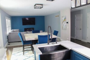 Une cuisine moderne avec un îlot central, un coin repas avec des chaises bleues et un canapé gris.