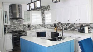Een moderne keuken met witte kastjes, een blauw eiland, een roestvrijstalen afzuigkap en een zwart-wit achterwand.