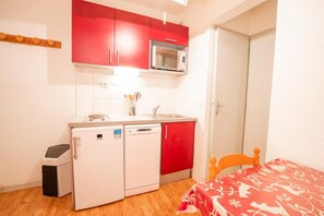 Una cocina compacta con armarios rojos, un microondas, un lavabo y un lavavajillas pequeño.