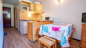 Cocina compacta con armarios de madera, microondas y refrigerador. Una pequeña mesa de comedor con mantel colorido se encuentra en el centro.