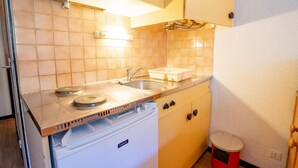 Cocina compacta con estufa, lavamanos y refrigerador pequeño.