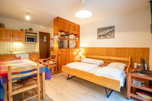 A cozy room with a wooden bed, a dining table, a kitchen area, and a bookshelf.
