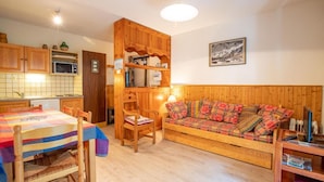 Un salon chaleureux avec un canapé en bois, une table à manger avec des chaises et un coin cuisine doté de meubles en bois et d’un four à micro-ondes.