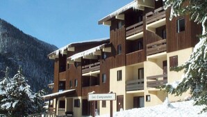Un immeuble à plusieurs étages doté de balcons, entouré d’arbres couverts de neige et avec une chaîne de montagnes en arrière-plan.
