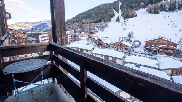A wooden balcony with a view of a snow-covered town, buildings, and a ski lift.