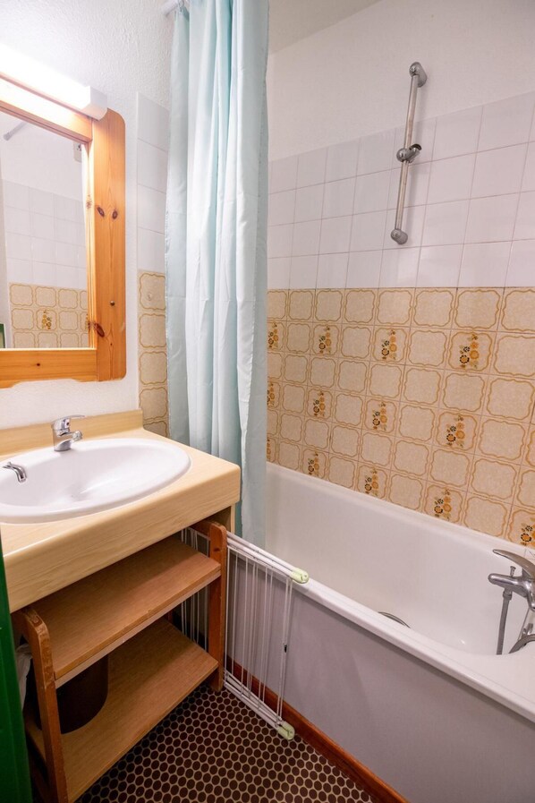 A bathroom with a wooden vanity, a white sink, a mirror, a shower with a glass door, and a tiled wall with a floral pattern.