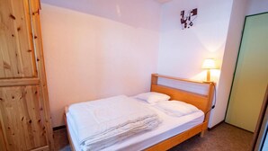A single bed with a wooden frame and white bedding, a bedside lamp, and a wall with a geometric artwork.