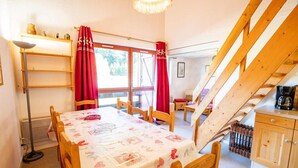 A cozy dining area with a table set for four, wooden chairs, a red curtain, and a staircase leading to an upper level. - 100m from ski slopes, 2nd floor, balcony, parking, tv, 47m², La Norma (La Norma)