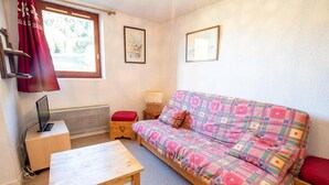 A cozy room with a wooden table, a plaid sofa, a red cushion, a small wooden chest, and a laptop on a side table. - 100m from ski slopes, 2nd floor, balcony, parking, tv, 47m², La Norma (La Norma)