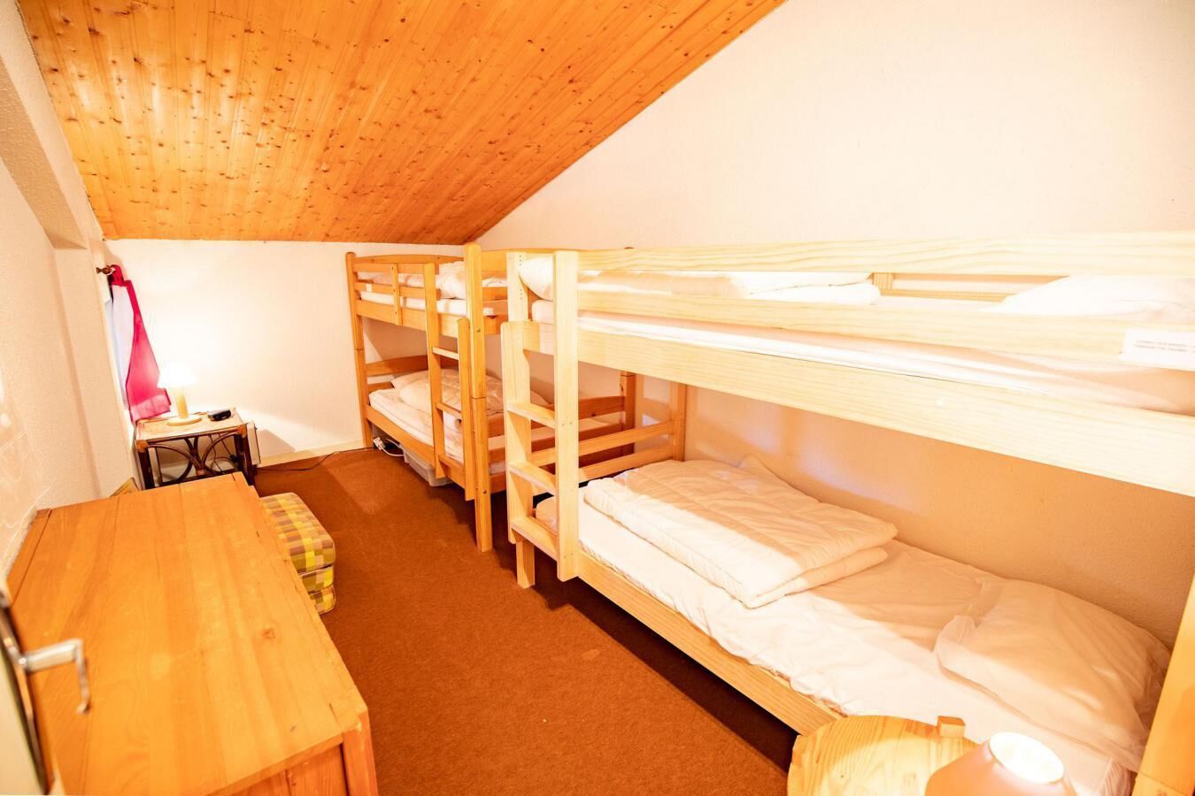A dormitory room with bunk beds, a wooden desk, and a small table with a lamp.