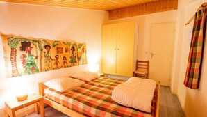 A bedroom with a bed, a small table, a chair, a wardrobe, and a tapestry on the wall. - 280m from resort center, 1st floor, balcony, parking, tv, 47m², La Norma (La Norma)