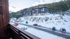 Un edificio in legno con un balcone che si affaccia su una strada innevata, con auto e un altro edificio sullo sfondo.