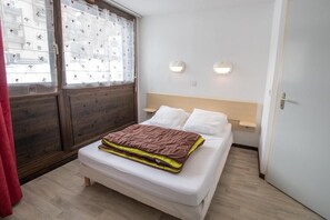 A bedroom with a bed, a wooden headboard, a window with a view of buildings, and two wall-mounted lights. - 300m from ski slopes, Ground floor, terrace, parking, tv, ski locker, 45m², La Norma (Villarodin-Bourget)