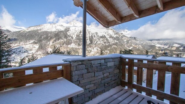 Une terrasse en bois avec un mur en pierre, offrant une vue sur un paysage montagneux enneigé.