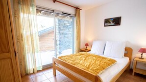 Une chambre à coucher avec un lit en bois, une table de chevet avec une lampe, une fenêtre avec des rideaux et un tableau accroché au mur.