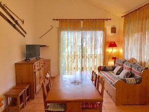 A cozy living room with a wooden dining table, sofa, and TV. - Chalet, 300m from resort center, Ground floor, balcony, parking, tv, ski locker, 45m², La Norma (La Norma)