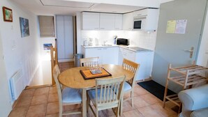 Une cuisine compacte avec des meubles blancs, un four à micro-ondes et un évier. On y trouve une table à manger en bois, des chaises et un petit tapis.