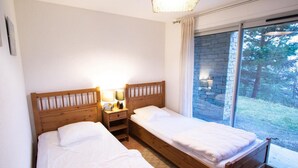 Une chambre à coucher avec deux lits en bois, une table de chevet avec des lampes et une fenêtre donnant sur des arbres.