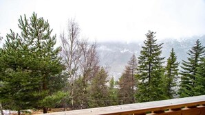 Une terrasse en bois surplombe une zone boisée et offre une vue sur les montagnes au loin.
