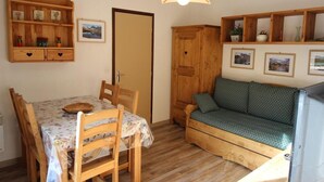 A cozy room with a wooden dining table, chairs, a sofa, and a cabinet with shelves. - 130m from ski slopes, 3rd floor, balcony, parking, tv, ski locker, 35m², La Norma (La Norma)