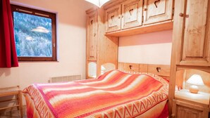 A bedroom with a bed, wooden cabinets, a window with a view of trees, and a red curtain. - 130m from ski slopes, 3rd floor, balcony, parking, tv, ski locker, 35m², La Norma (La Norma)
