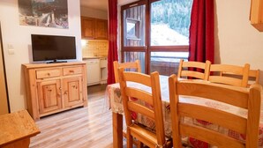 A cozy room with a wooden dining table, chairs, a television on a wooden cabinet, and a window with a view of a snowy landscape. - 130m from ski slopes, 3rd floor, balcony, parking, tv, ski locker, 35m², La Norma (La Norma)