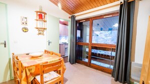 Ein gemütlicher Essbereich mit Holztisch und -stühlen, eine Küche im Hintergrund und eine große Schiebeglasdoor zum Balkon mit Blick auf eine verschneite Landschaft.
