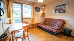 Una sala acogedora con una mesa de comedor de madera, sillas, un sofá estampado y un pequeño estante con adornos.