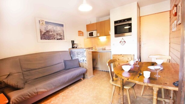 Un espacio habitable compacto con sofá, una mesa de comedor con sillas, una zona de cocina con armarios y electrodomésticos, y un cuadro en la pared.