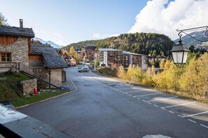 A street view with a stone building on the left, a row of modern buildings in the center, and a mountain in the background.