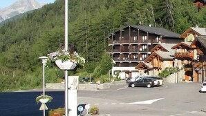 Et fjeldhotel med flere træbalkoner, en parkeringsplads og udsigt til et bjerg.