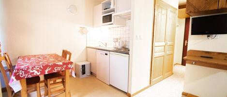 A compact kitchen with a microwave, sink, and cabinets. There is a dining table with chairs and a small refrigerator.
