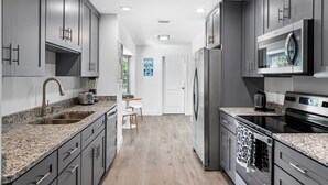 A modern kitchen with granite countertops, stainless steel appliances, and dark gray cabinetry. - Sunny House with heated pool, 12min drive to Engelwood Beach, Port Charlotte FL (Port Charlotte)