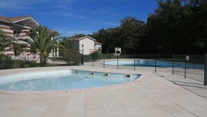 A swimming pool with a tiled deck, surrounded by a fence, and adjacent to residential buildings.