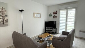 A living room with two grey sofas, a wooden coffee table, a television, and a small wooden stool.