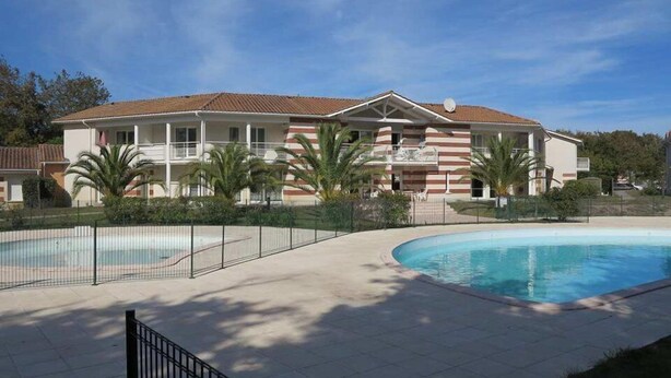 A hotel with a swimming pool, palm trees, and a clear blue sky.
