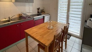 A compact kitchen with a wooden table, red cabinets, and a window with blinds.