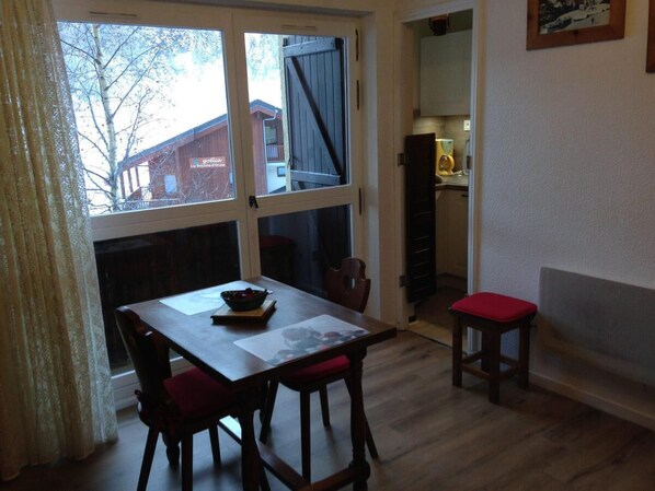 Un comedor con una mesa y sillas, una ventana que ofrece vista a un edificio, y un taburete pequeño.