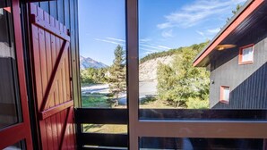 A view from a room with a large window overlooking a mountainous landscape, a wooden door, and a small window with a red frame. - 100m from ski slopes, 2nd floor, balcony, parking, tv, 54m², La Norma (La Norma)
