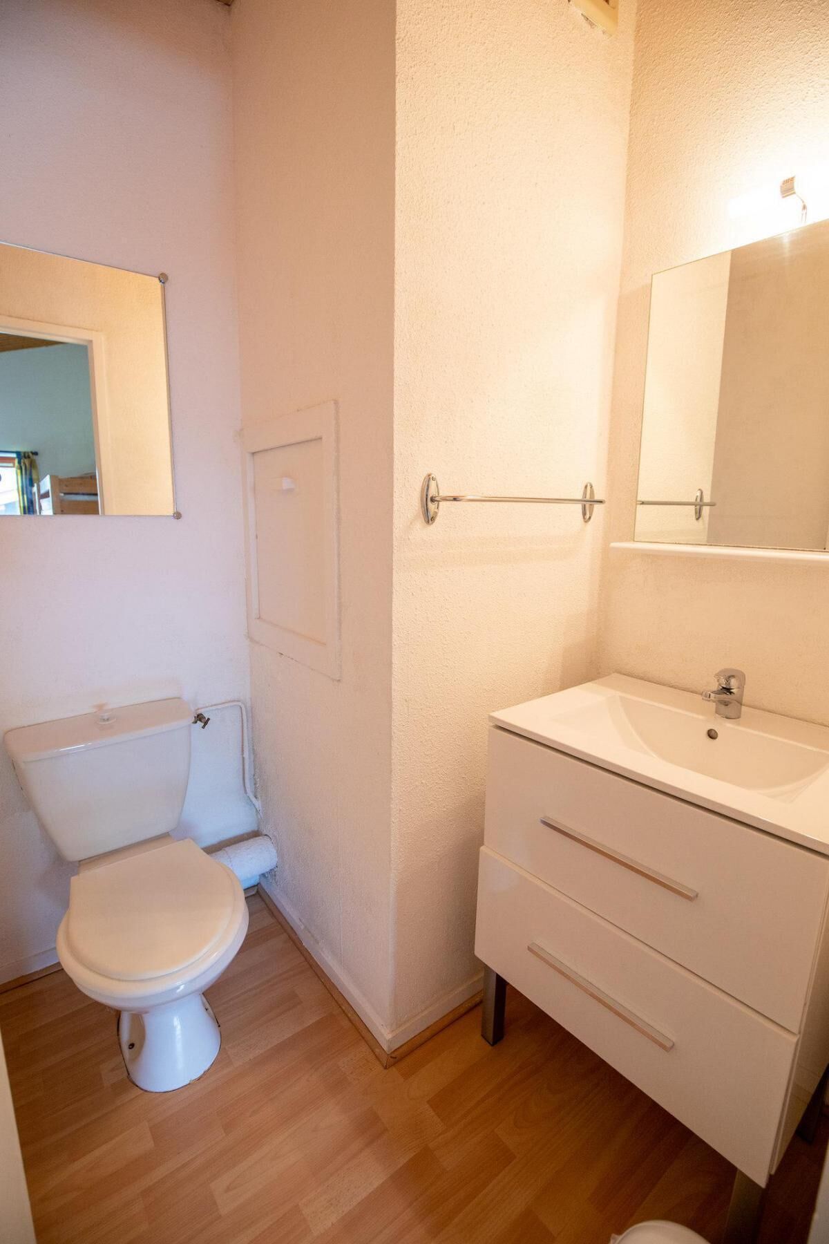 Une petite salle de bain propre, équipée de toilettes, d’un lavabo et d’un miroir.