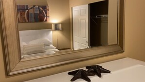 Habitación de hotel con un espejo grande, una cama con ropa de cama blanca, una mesita de noche con una lámpara y una decoración de estrella de mar en la encimera.
