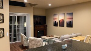 Una sala de estar con chimenea, una mesa de centro de vidrio, un sofá y un televisor instalado en la pared.