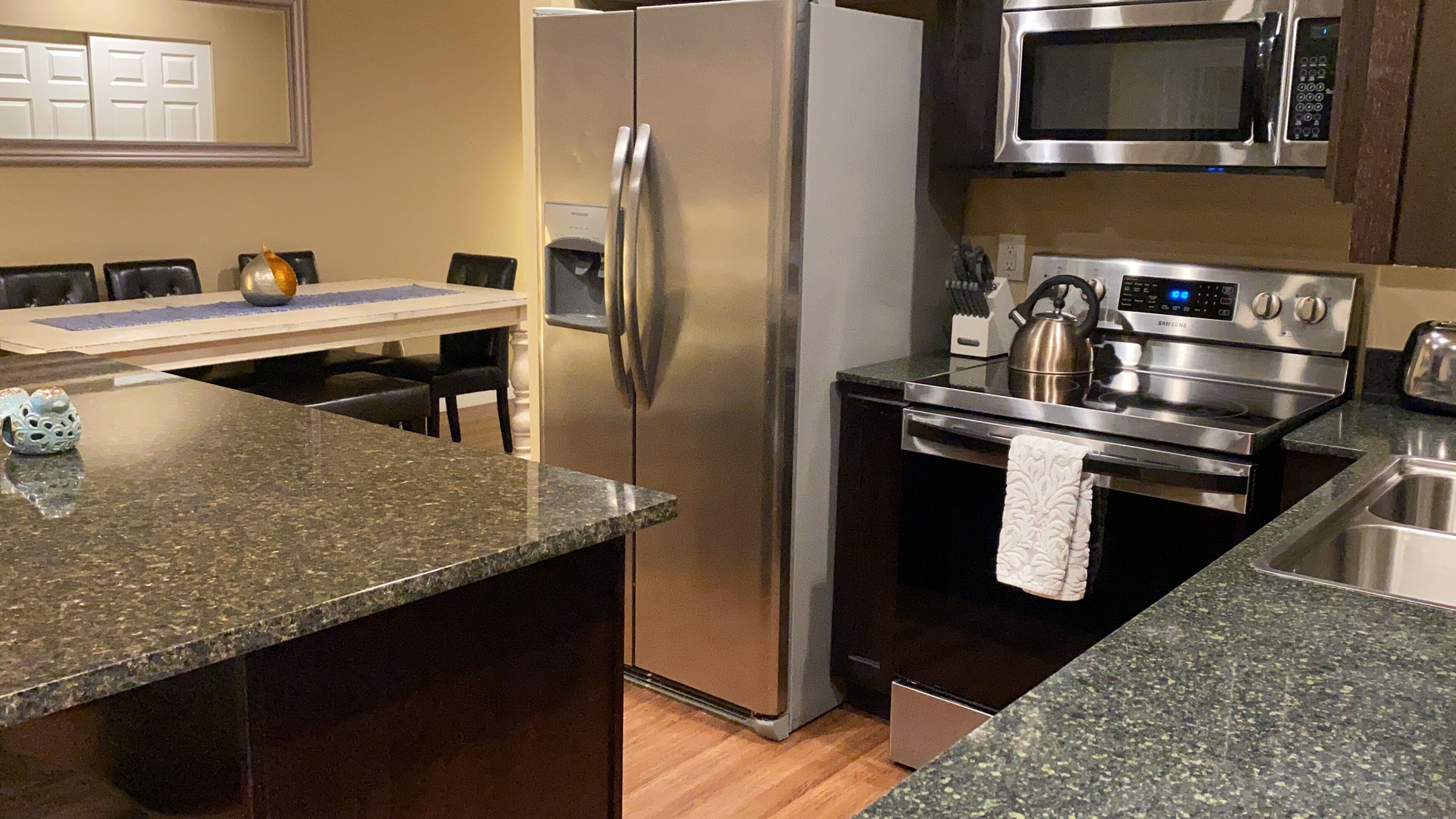 A kitchen with a stainless steel refrigerator, a microwave, a Samsung oven, and granite countertops.