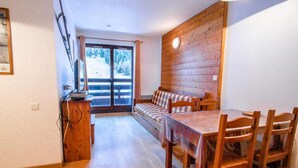 Un intérieur en bois comprenant une table et des chaises, un canapé, et une vue sur un espace extérieur accessible par une porte vitrée.