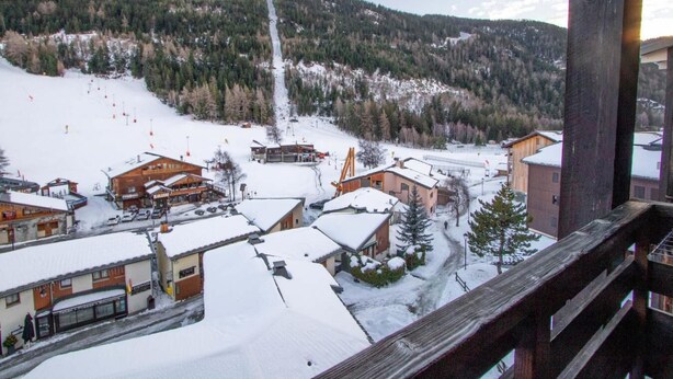 Une ville de montagne enneigée, avec des bâtiments, un télésiège et une vue dégagée sur la forêt environnante.