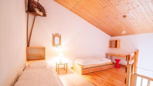 A small, cozy bedroom with a sloped ceiling, a single bed, a bedside table with a lamp, a small stool, and a wooden bench. - 280m from resort center, 1st floor, balcony, parking, tv, 54m², La Norma (La Norma)