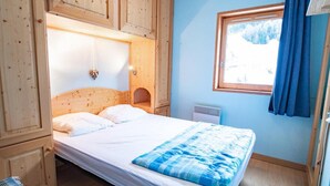 A bedroom with a wooden headboard, a bed with white bedding, a window with a view of trees, and a blue curtain. - 130m from ski slopes, 4th floor, balcony, parking, tv, ski locker, 35m², La Norma (La Norma)