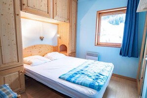 Cozy bedroom with a single bed, wooden headboard, and a window offering a view of the surrounding snowy landscape.